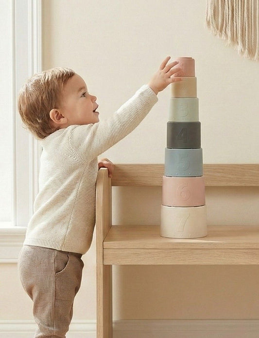 Toddler stacking NARA silicone stacking cups into a tower on a wooden table — set of 7 numbered cups in muted Scandi tones