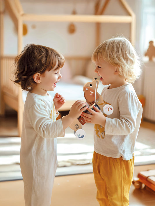 Two toddlers playing together with the Speedy Monkey Puppy Pull Along — FSC certified wooden pull-along toy for 12 months+, in a warm Scandi nursery setting.