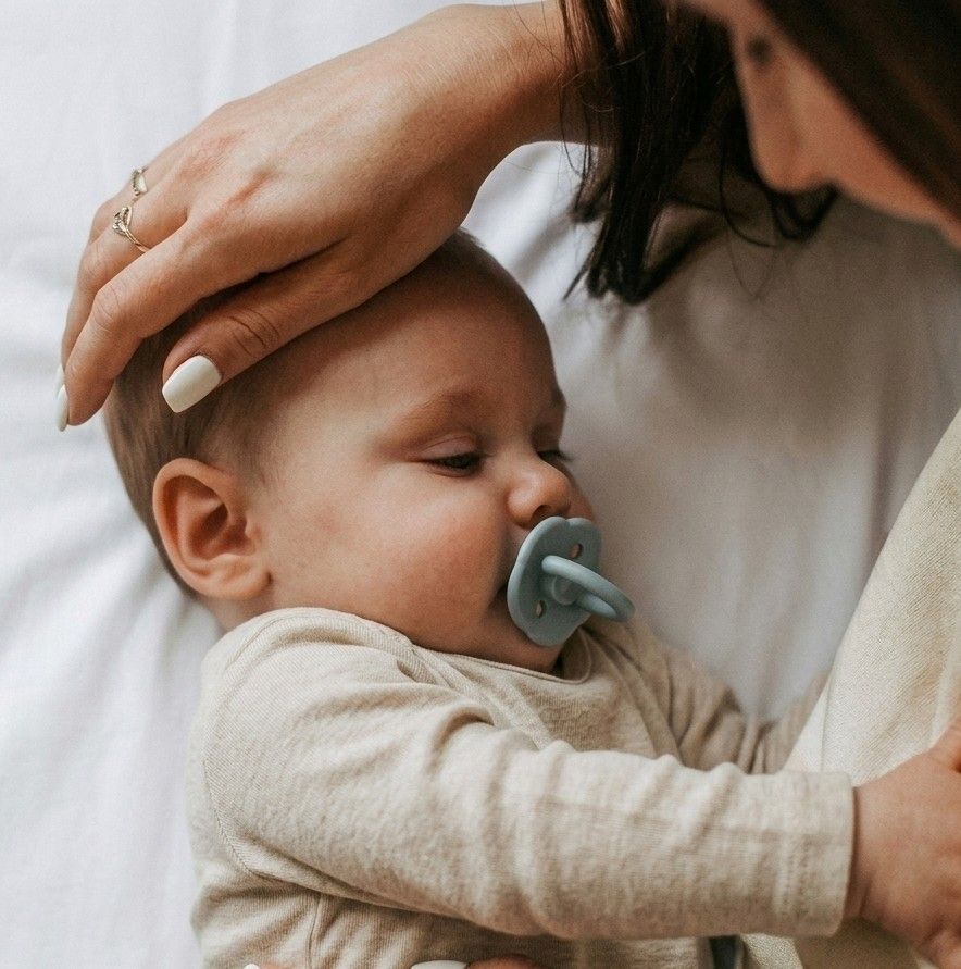 Mother cradling a sleeping newborn baby using a NARA silicone pacifier in Ether