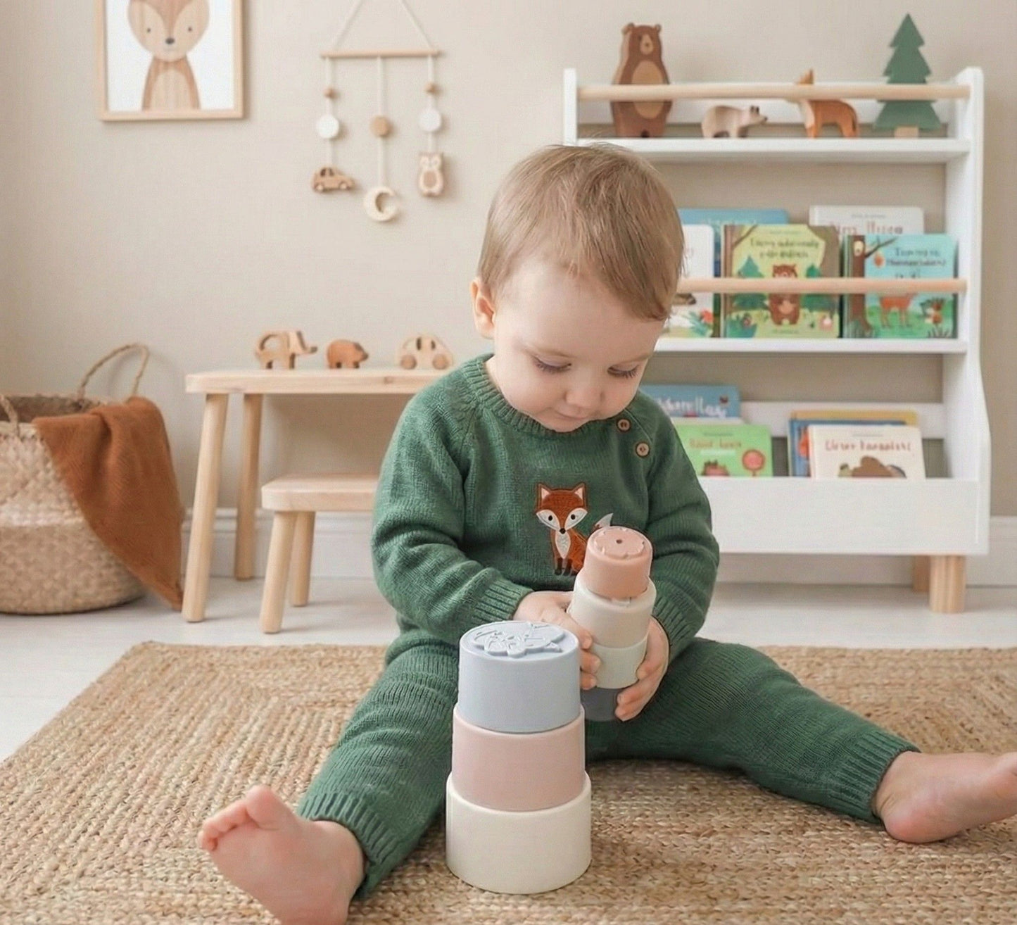 Baby playing with NARA silicone stacking cups on a jute rug in a Scandi-style nursery