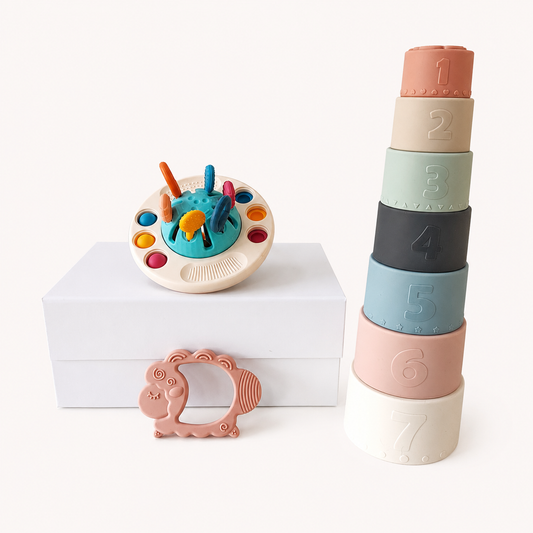 NARA Silicone Grow & Play Gift Set flatlay — NARA Little UFO sensory toy on white gift box, seven silicone stacking cups numbered 1–7 in muted tones, and silicone lamb teether, cream background
