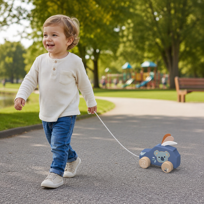 Smiling toddler pulling the Speedy Monkey Pull-Along Car through a park — blue koala wooden pull-along toy, FSC certified personalised baby gift by NARA
