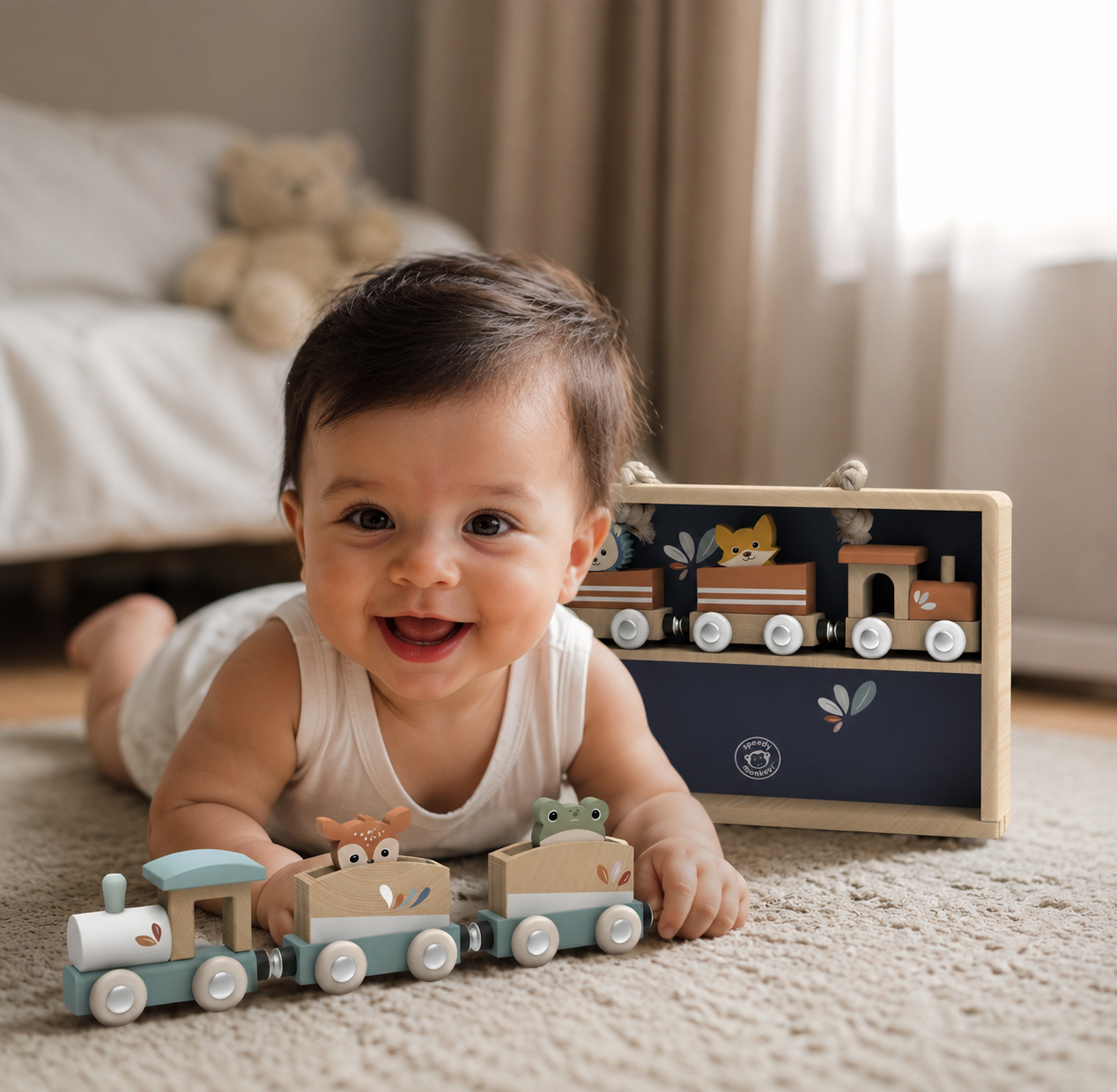 Smiling baby lying next to the Speedy Monkey Personalised Train Stacker and navy display case — wooden animal train set with fox, frog and deer carriages, FSC certified personalised baby gift by NARA